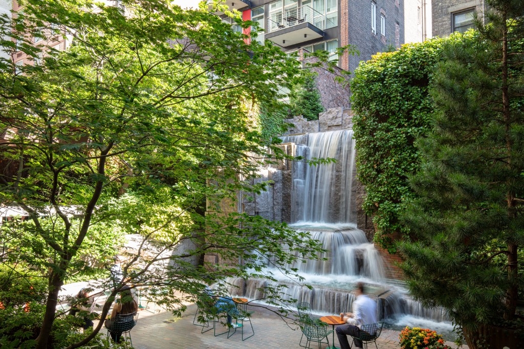 The 25-foot waterfall at Greenacre Park cascading over tiered granite blocks, framed by trees and ivy, with visitors seated at tables in front