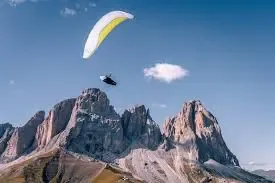 Person paragliding over rocky mountain peaks under a clear blue sky