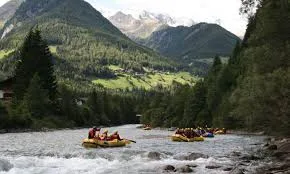 Groups of people rafting on a river surrounded by forested mountains under daylight