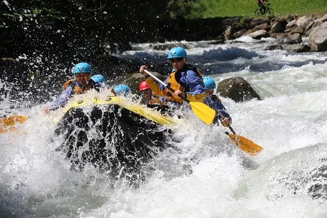 Group wearing helmets and life jackets paddling through turbulent river rapids in inflatable raft